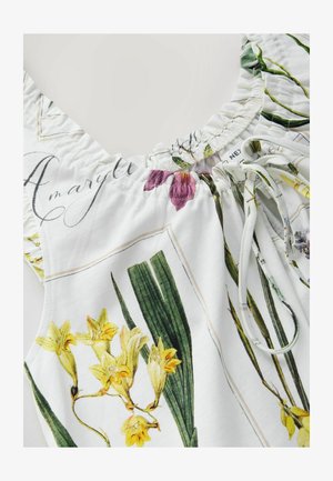 Květinová halenka s bílým pozadím, zdobená žlutými a fialovými květinovými vzory, se shrnutým výstřihem a nastavitelným stahovacím detailem.