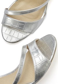 Silberne Sandalen aus Kunstleder mit überkreuzten Riemen, die ein strukturiertes Krokodileder-Muster aufweisen und ein rundes, offenes Zehendesign haben.