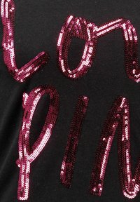 T-shirt nera con grande lettering in paillettes rosa lucido in un design ondulato, che spellano "LOVIN". Il tessuto è liscio e stretch.