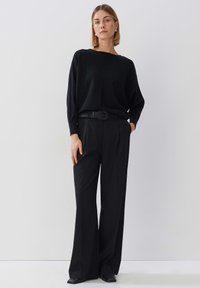 Schwarzer Strickpullover mit weitem Ausschnitt, kombiniert mit hochgeschnittenen, taillierten schwarzen Hosen. Enthält einen gewebten schwarzen Gürtel und elegante schwarze Schuhe.