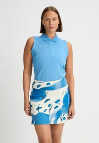 Blå ärmlös polo med krage, i kombination med en kjol i vitt och blått med mönster av abstrakta former och ett flödande design.