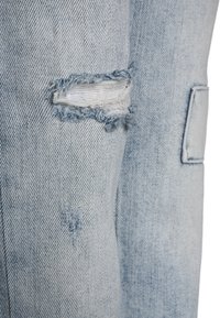 Jeans de denim azul claro desgastados que presentan desgarros en las rodillas deshilachados, un desvanecido sutil y una textura suave, con un parche en el lateral.