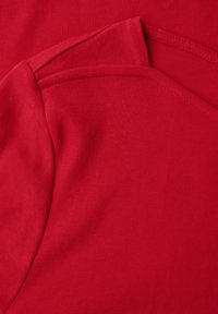 Červená bavlněná košile s hladkým povrchem, která má dvouvrstvý výstřih a detaily švů, zdůrazňující její strukturovaný design.