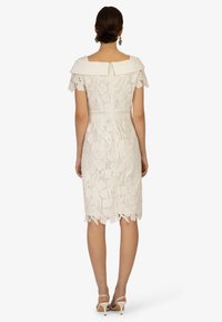 Abito bianco in pizzo con colletto off-the-shoulder, maniche corte, motivo floreale, vita aderente, orlo al ginocchio con bordo a scallop e chiusura con zip.