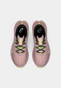 Zapatillas de running de color rosa claro con parte superior texturizada, cordones negros y detalles amarillos. Cuentan con una suela acolchada y logotipos de la marca en la lengüeta.