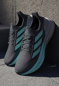 Gray athletic shoes with a textured upper, featuring teal accent stripes, round laces, and a light green sole with "Light Boost" branding.