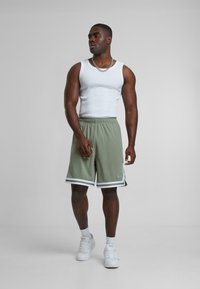 Green athletic shorts with white side stripes, paired with a white tank top. The shorts feature an elastic waistband and a casual fit.