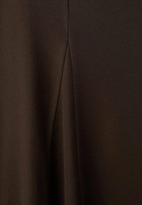 Tejido marrón oscuro con una textura suave que presenta un detalle de costura a lo largo del borde. El diseño exhibe una silueta simple y elegante.