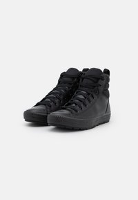 Black high-top sneakers featuring a smooth leather upper, textured lace closures, and a grooved rubber sole. Minimalistic design with padded collar.