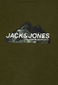 Sötétzöld szövet hegy grafikával és vastag fehér "JACK & JONES" felirattal, valamint kisebb szöveggel: "KONSTRUKCIÓS_INNOVATÍV_HASZNÁLAT".