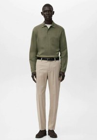 Tricou polo cu mânecă lungă verde măsliniu, cu guler, asortat cu pantaloni bej croiți și pantofi maro, stilizat cu o curea neagră.