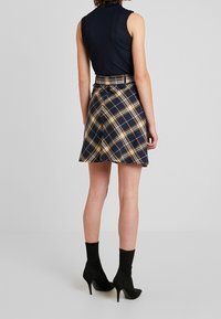 Gonna a righe navy con accenti gialli e bianchi, caratterizzata da un design plissettato e una vita con cintura. Indossata con stivaletti neri con tacco alto.