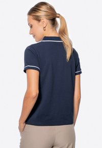 Polo shirt blu navy con maniche corte e rifiniture bianche su colletto e polsini. Vestibilità classica, tessuto morbido, dotato di fessure laterali per facilitare i movimenti.