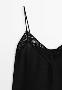 Camisole noire avec fines bretelles et un col orné de dentelle. Le tissu est lisse, tandis que la dentelle présente un motif complexe.
