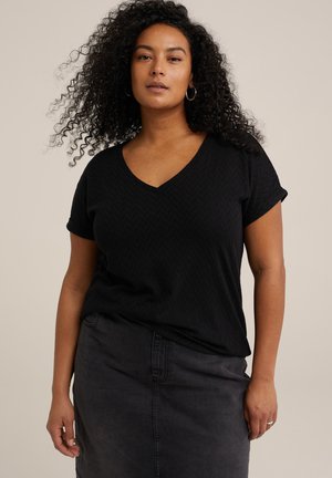 Black short-sleeve V-neck top with a textured chevron pattern, paired with a fitted dark gray denim skirt. Curly hair and simple hoop earrings.