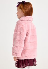Giacca in finta pelliccia rosa con un ampio colletto, texture a righe orizzontali e vestibilità morbida. Abbinata a una gonna di pizzo bordeaux a strati.
