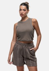 Bruine cropped tanktop met witte stiksels, gecombineerd met bijpassende bruine shorts met een elastische tailleband en zijzakken.