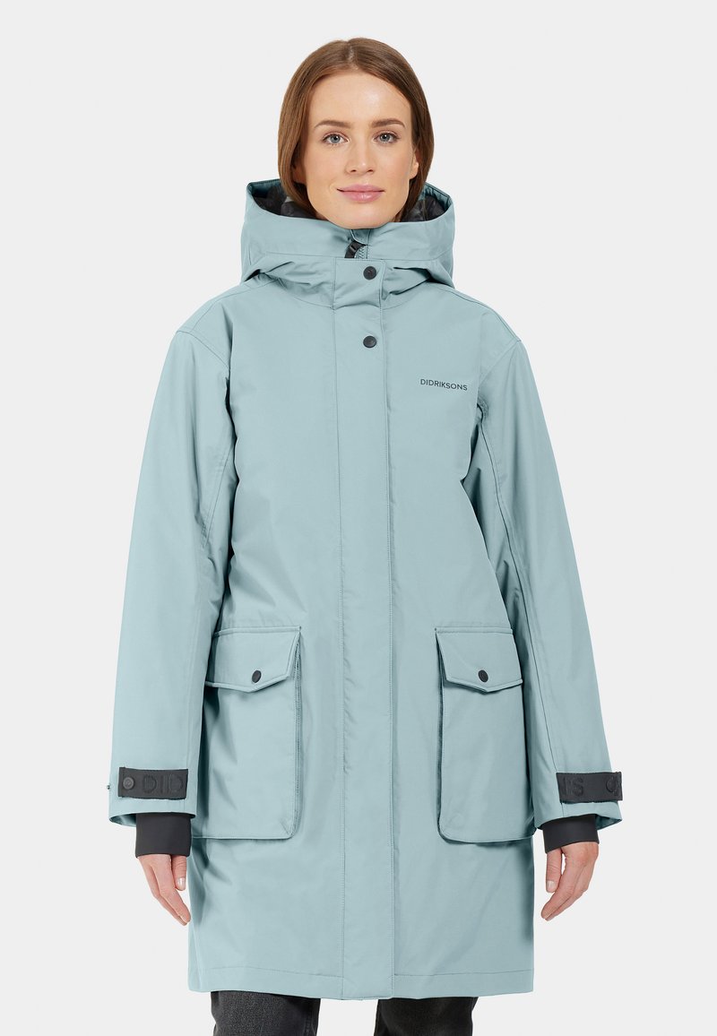 Ljusblå vattentät parka med huva, tryckknappar, två framfickor och svarta detaljer vid ärmsluten. Designad för användning i kallt väder.