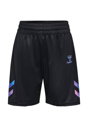 Jong roodharig meisje in een roze en blauwe sporttrui met nummer 12, zwarte korte broek, witte sokken en zwarte sneakers, staand tegen een effen achtergrond.