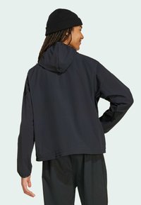 Crna kapuljača jakna izrađena od tkanine s glatkom teksturom. Ima duge rukave i opušteni kroj. Vidljivo šivanje duž obruča.