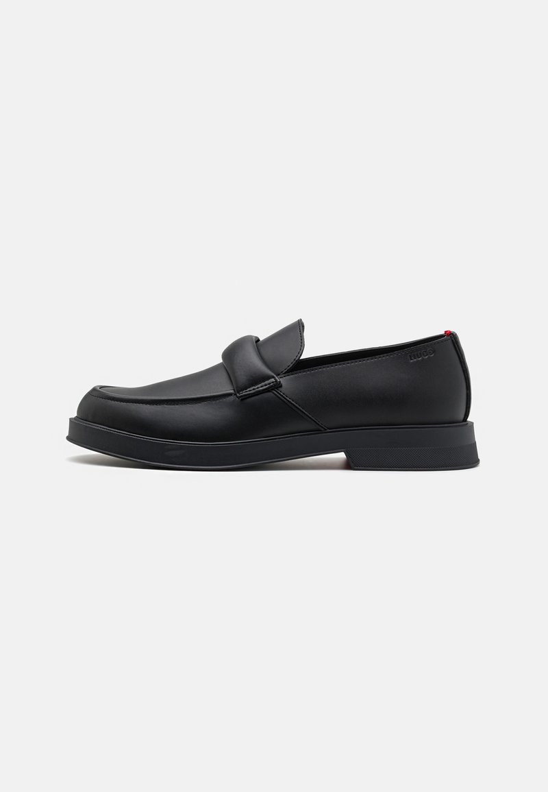 Mocassins en cuir noir avec une finition lisse, légèrement arrondie à l'avant, accent de sangle à l'avant et une semelle en caoutchouc texturée basse. Logo à l'arrière.