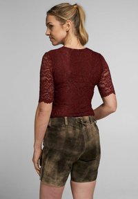 Burgunder Spitzenoberteil mit kurzen Ärmeln und gewellten Kanten, kombiniert mit braunen Wildledershorts, die eine strukturierte Optik und ein Rückengurt-Detail zeigen.