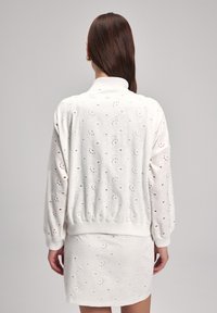 Completo bianco lavorato a maglia, composto da una maglietta con collo aperto sul retro e una gonna aderente, entrambi con motivi floreali a occhielli e polsini a coste.