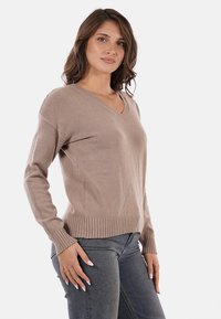 Maglione beige a scollo a V realizzato in morbido materiale, con polsini e orlo a costine, abbinato a jeans grigi aderenti.