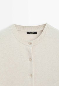 Cardigan en maille beige avec col rond et trois boutons assortis sur le devant. Tissu doux et texturé.