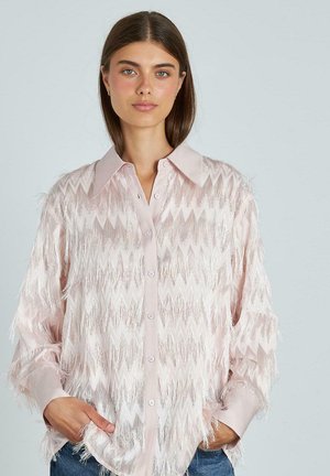 Camisa de botones de color rosa claro con un patrón de zigzag, que presenta un fleco texturizado a lo largo de las mangas y el cuerpo, confeccionada en una tela suave y brillante.