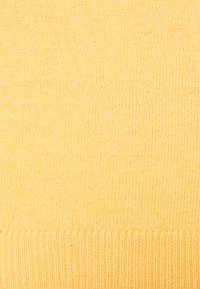 Pull en tricot jaune présentant un tissu doux et texturé avec un ourlet côtelé. Design léger et sans coutures, de couleur uniforme.
