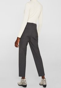 Pantalon gris ajusté à jambes droites, en tissu texturé, avec des poches latérales. Associé à un haut crème à côtes et des bottines à motifs.