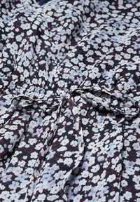 Bloemendress in donkere stof met witte en kastanjebruine patronen, voorzien van een strik taille, plooien en een zachte, lichte textuur.