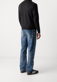 Sweat-shirt noir avec poignets et ourlet côtelés, associé à un jean droit bleu délavé et des baskets noires à rayures blanches.