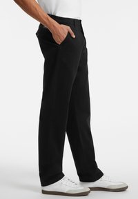 Schwarze Baumwollhosen mit gerade geschnittenem Bein, ausgestattet mit Seitentaschen und einem Taillenbund. Kombiniert mit weißen Sneakers für den Kontrast.