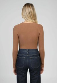 Haut marron à manches longues côtelées, associé à un jean taille haute bleu foncé, présentant une silhouette ajustée et un design minimaliste.