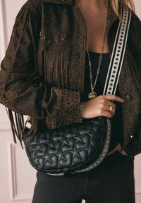 Fekete steppelt táska csillagmintával és csíkos pánttal, egy barna leopárdmintás dzseki közelében, amely rojtos és ezüst díszítéseket tartalmaz.