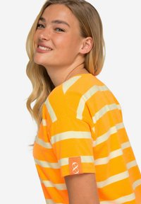 Camiseta a rayas naranja y amarilla hecha de tela suave, con mangas cortas y un logo en el puño.