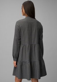 Zwart blauw geruite jurk met een gelaagde rok, lange mouwen en een rugpand, gemaakt van gestructureerde stof. Heeft een losse pasvorm.