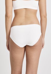 Weiße Baumwollunterwäsche mit einem gewellten Spitzenrand am Bund, die eine glatte, weiche Textur und eine klassische Slipform aufweist.