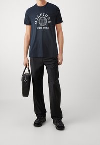 Námořnické bavlněné tričko s bílým potiskem "HILFIGER NEW YORK", spárované s černými kalhotami a nesoucí černou strukturovanou tašku.