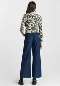 Langarm top met luipaardprint in beige, groen en zwart, gecombineerd met wijde spijkerbroek van donkerdenim. Heeft zakken en een comfortabele pasvorm.