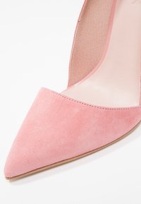 Chaussure à talon haut en suède rose à bout pointu avec une semelle intérieure lisse et un bord de semelle marron clair sur fond blanc.