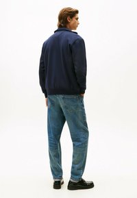 Felpa navy con polsini e orlo a coste, abbinata a jeans in denim azzurro chiaro. Scarpe nere con texture liscia e dettagli sottili.