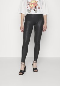 Svart ormskinnsmönstrade leggings i ett stretchigt, glansigt material; har en mjuk yta och en hög midja, kombinerat med svarta klacksandaler.