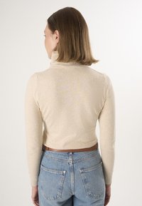 Cremefarvet, tætsiddende turtleneck sweater med lange ærmer, parret med højtaljede lyseblå jeans. Glat tekstur, cropped kant.