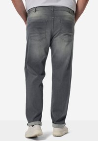Grå denimjeans för män med avslappnad passform, med två bakfickor och subtil blekning. Uppvikta avslut avslöjar vita sneakers.