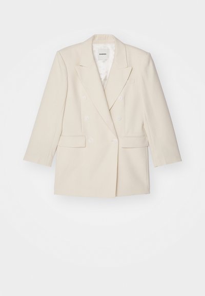 Doppelreihige Blazer aus leichtem Creme-Stoff mit glatter Textur, mit Revers und zwei Fronttaschen. Mit weißen Knöpfen ausgestattet.