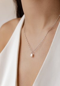 Collar de plata con un diseño de cadena retorcida, que presenta un colgante de perla blanca, situado alrededor del área de la clavícula.