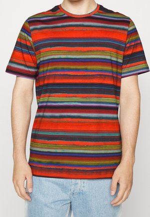 Man die een T-shirt met korte mouwen draagt met horizontale strepen in oranje, groen, blauw, paars en zwart, gecombineerd met lichtblauwe spijkerbroek.